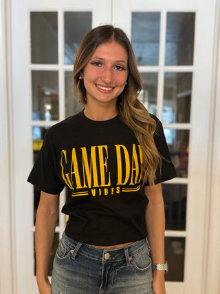 Person wearing a black t-shirt with 'GAME DAY VIBES' in yellow text, standing indoors.