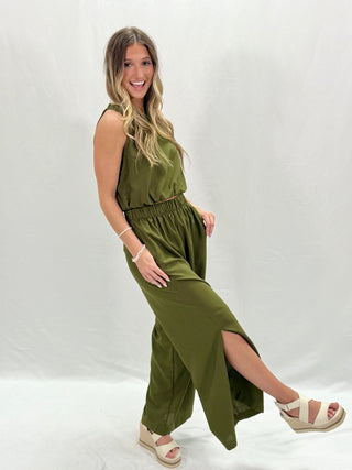 A female model wearing an olive green sleeveless set with a high slit on the side.