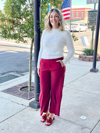 A person standing on a sidewalk wearing burgundy high waist wide pants with a white top and red shoes.