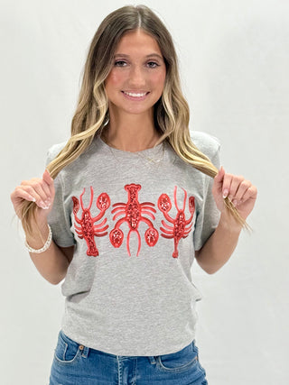 A person wearing a gray t-shirt with three red faux sequin crawfish designs on the front.