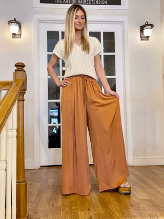 A person standing on a staircase wearing camel-colored elastic waist pants and a beige top.