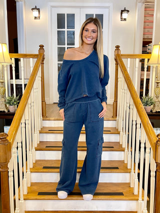 A woman standing on a staircase wearing dark indigo pants with a matching top, posing with a smile.