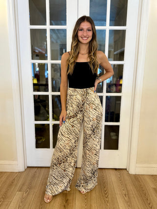 Woman wearing a black top and patterned pants standing in front of a glass door.