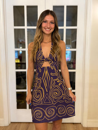 Woman wearing a purple dress with gold patterns standing in front of a glass door.