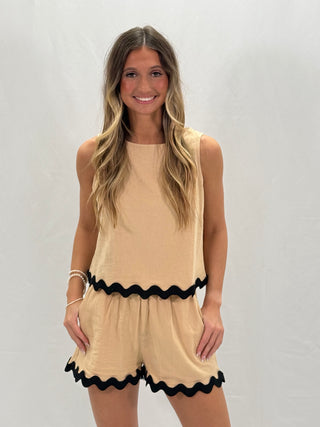 A woman wearing a beige sleeveless top and shorts set with black rickrack detailing on the hem.