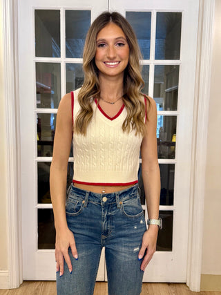 A woman wearing a V Neck Ivory Red Sweater Vest with a white and red striped neckline, paired with blue jeans.