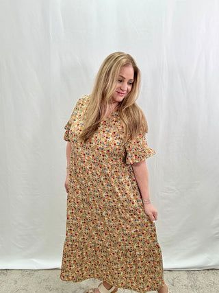 A woman wearing a beige floral print midi dress with short sleeves and a V-neck neckline.