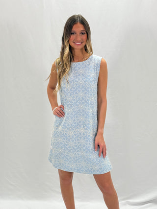A woman standing and smiling, wearing a blue floral mini dress with embroidery.