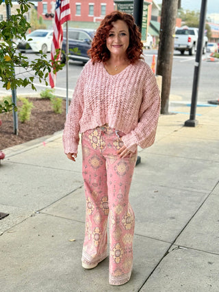 Woman wearing a pink patterned outfit standing on a sidewalk with a city street background.