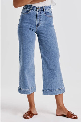 A pair of high-waisted, cropped wide leg blue denim jeans with back patch pockets and a button waistband.