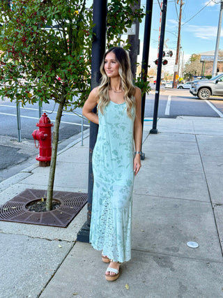 A woman standing on a sidewalk next to a fire hydrant, wearing a sleeveless knee-length dress with a floral print and lace detailing.