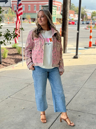 Woman wearing a pink denim jacket, white graphic t-shirt, and blue jeans on a sidewalk.
