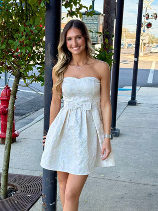 A woman wearing a cream pink floral strapless dress standing on a sidewalk.