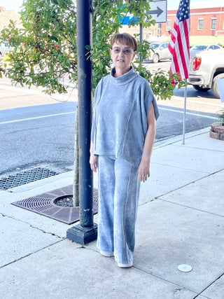 A person standing on the sidewalk next to a flag pole, wearing denim blue wide leg pants and a grey top.