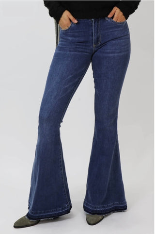 A pair of flare-style blue denim jeans on a model, with a focus on the leg and footwear.