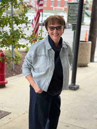 Person wearing sunglasses and a light denim jacket on a city street