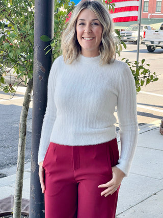 woman on sidewalk with cream sweater and red pants