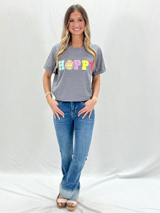 A woman standing in front of a white background, wearing mid-rise full inseam bootcut jeans with a contrast hem band design.