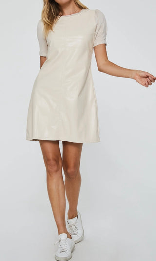 A woman wearing a beige knee-length dress with short sleeves, paired with white sneakers.