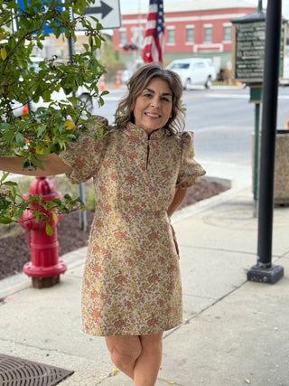 Woman in a floral dress standing on a sidewalk with a street and building in the background