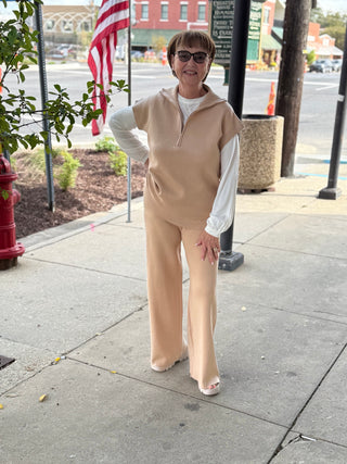 Woman in beige outfit standing on a sidewalk with a street and flags in the background
