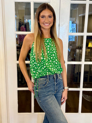 A person wearing a green and white sleeveless top with a pattern, paired with blue jeans.