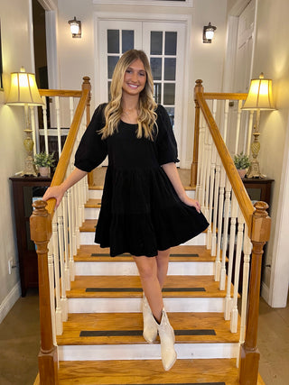 A woman standing on a staircase with a babydoll style dress on with grey colored stair ankle boots.