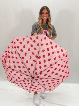 A person holding a compact umbrella with a pink background and red strawberry designs.
