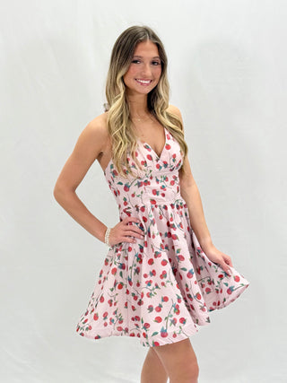A woman wearing a sleeveless mini dress with a floral and farm vibe print, standing against a neutral background.