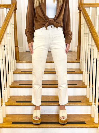 A person standing on a staircase wearing beige wheat jeans and a brown jacket with a white top.