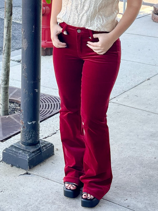 A person standing on the sidewalk wearing red high-waisted pants and a beige top.