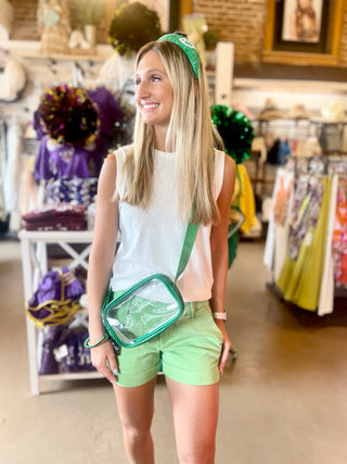 A person wearing a green and white outfit, specifically a green shirt and white shorts, standing in a retail environment with various clothes displayed in the background.