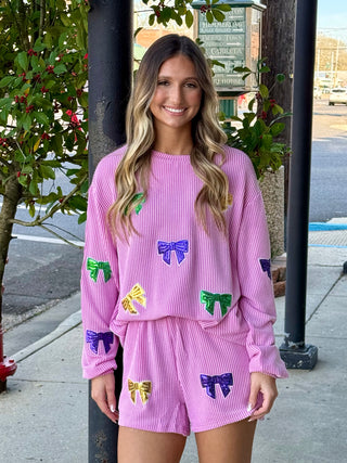 A woman wearing a pinkish/ purple outfit with colorful bow decorations standing on a sidewalk.