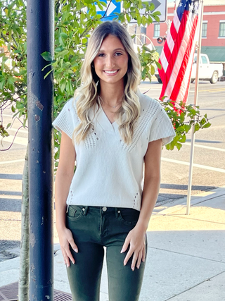 woman standing on sidewalk wearing a v-neck sweater vest with jean pants