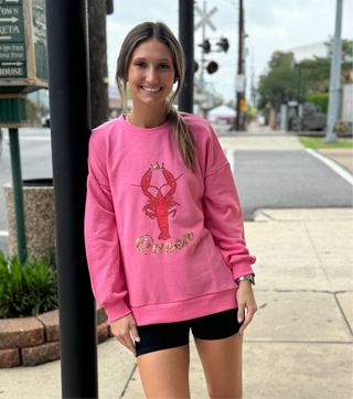 A person wearing a pink sweatshirt with 'Crawfish Queen' printed on the front.