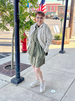 Older woman standing on the sidewalk, wearing a Cream jacket paired with a army green dress underneath