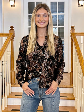 A woman standing on a staircase wearing a glittery, multicolored top with long sleeves and denim jeans.
