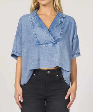 Woman wearing a blue denim top and black pants on a plain background