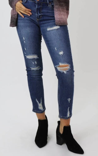 A pair of faded blue jeans with high waist and crocked design, paired with black boots and a purple multicolor sweater.