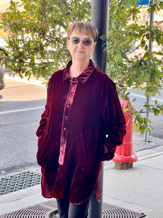 A woman standing next to a red fire hydrant, wearing a red long-sleeve button-down top with a collar, paired with black pants.