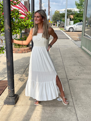A woman wearing white flowy dress with a lace top standing on a sidewalk.