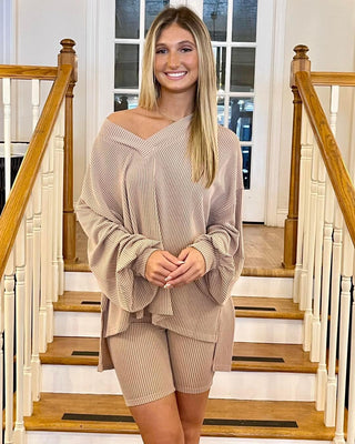A woman standing on a staircase wearing beige mocha 2 tone biker shorts and a matching loose-fitting beige top with a turtleneck.