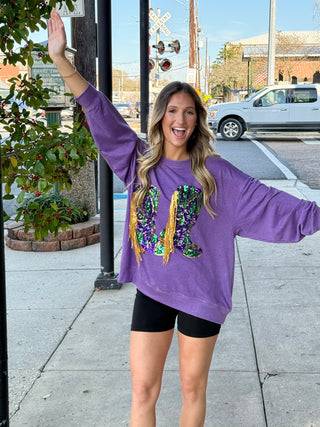 A woman wearing a purple pullover with fringe details. The pullover has Mardi Gras marching boot.