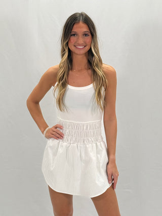 A woman wearing a white knit sleeveless romper with a smocked waist.