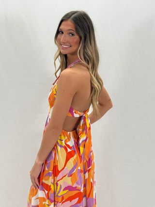 A model wearing a floral multicolored sleeveless dress with a halter neck and ruched detailing.