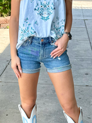 A pair of blue denim jean shorts with a floral top and white boots.