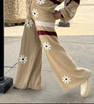 Beige sweater with white daisy patterns worn by a person on a sidewalk.