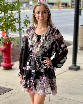 Woman wearing a floral dress with sheer sleeves on a city street.