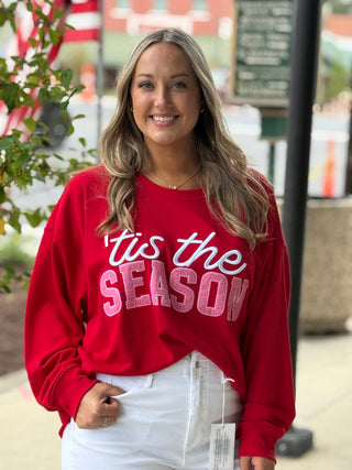 Woman wearing a red sweater with 'tis the season text outdoors.