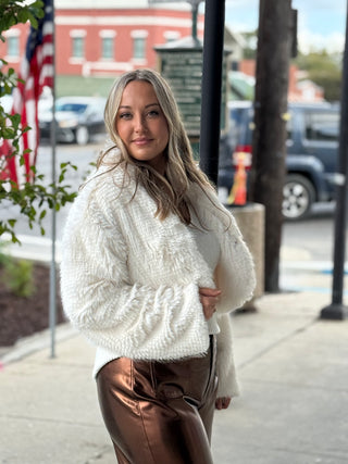 Woman wearing a white sweater and brown pants on a city street.